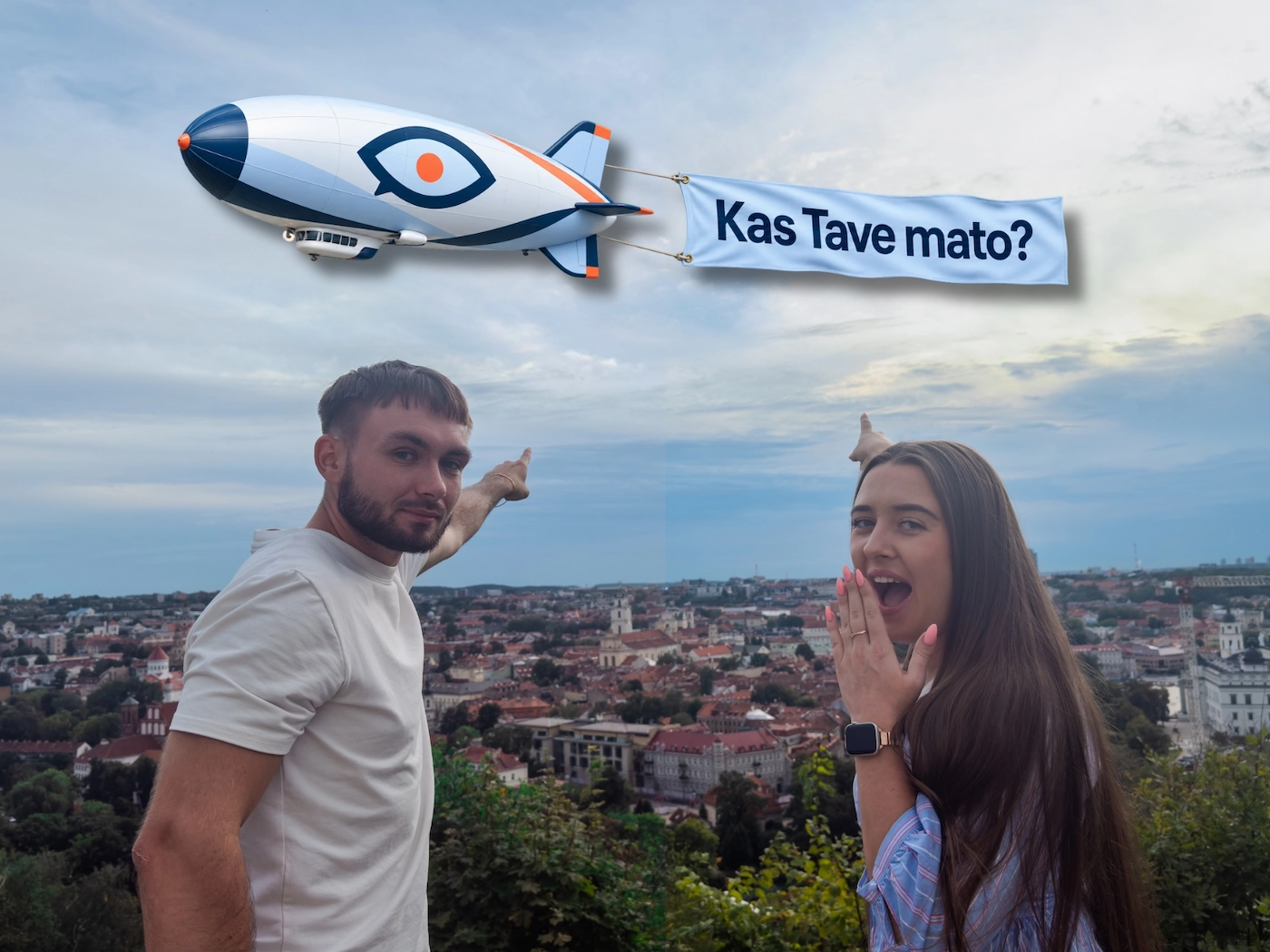 Kamilė ir Nojus Vilniaus panoramos fone rodo į dirižablį su užrašu „Kas Tave mato?“